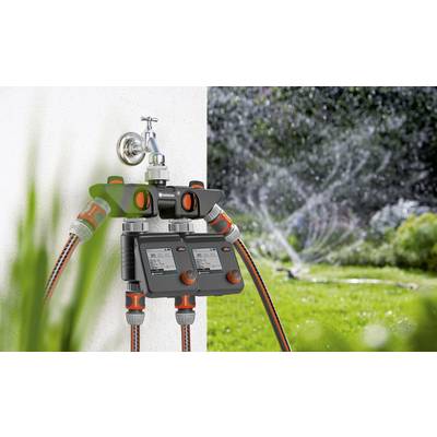 Ein automatisches Bewässerungssystem ist an einen Wasserhahn angeschlossen. Im Hintergrund läuft ein Rasensprenger auf einer grünen Fläche.