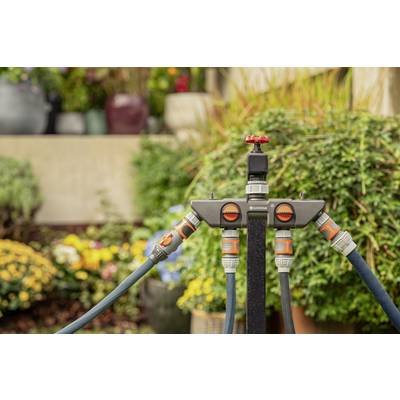 Gartenbewässerungssystem mit mehreren Anschlüssen und Ventilen, umgeben von bunten Blumen im Hintergrund.