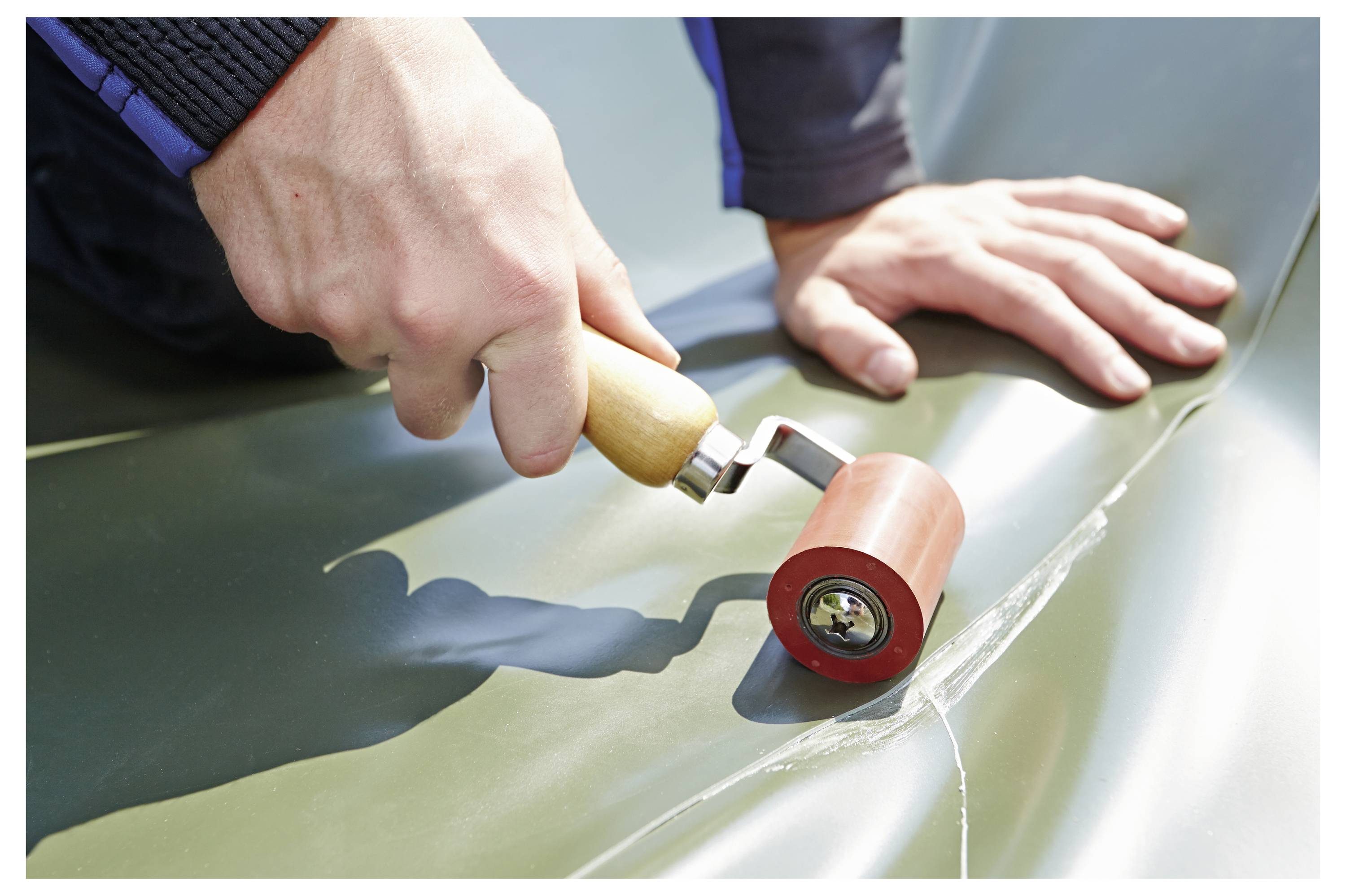 Eine Person, die einen Handroller verwendet, um eine Naht auf einer wasserdichten Plane zu versiegeln, wobei ein Schritt bei einer Bau- oder Reparaturaufgabe hervorgehoben wird.