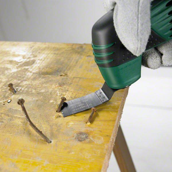 Eine Person verwendet ein Multifunktionswerkzeug mit einer oszillierenden Schneidklinge, um rostige Nägel aus einem Holzbrett zu entfernen.