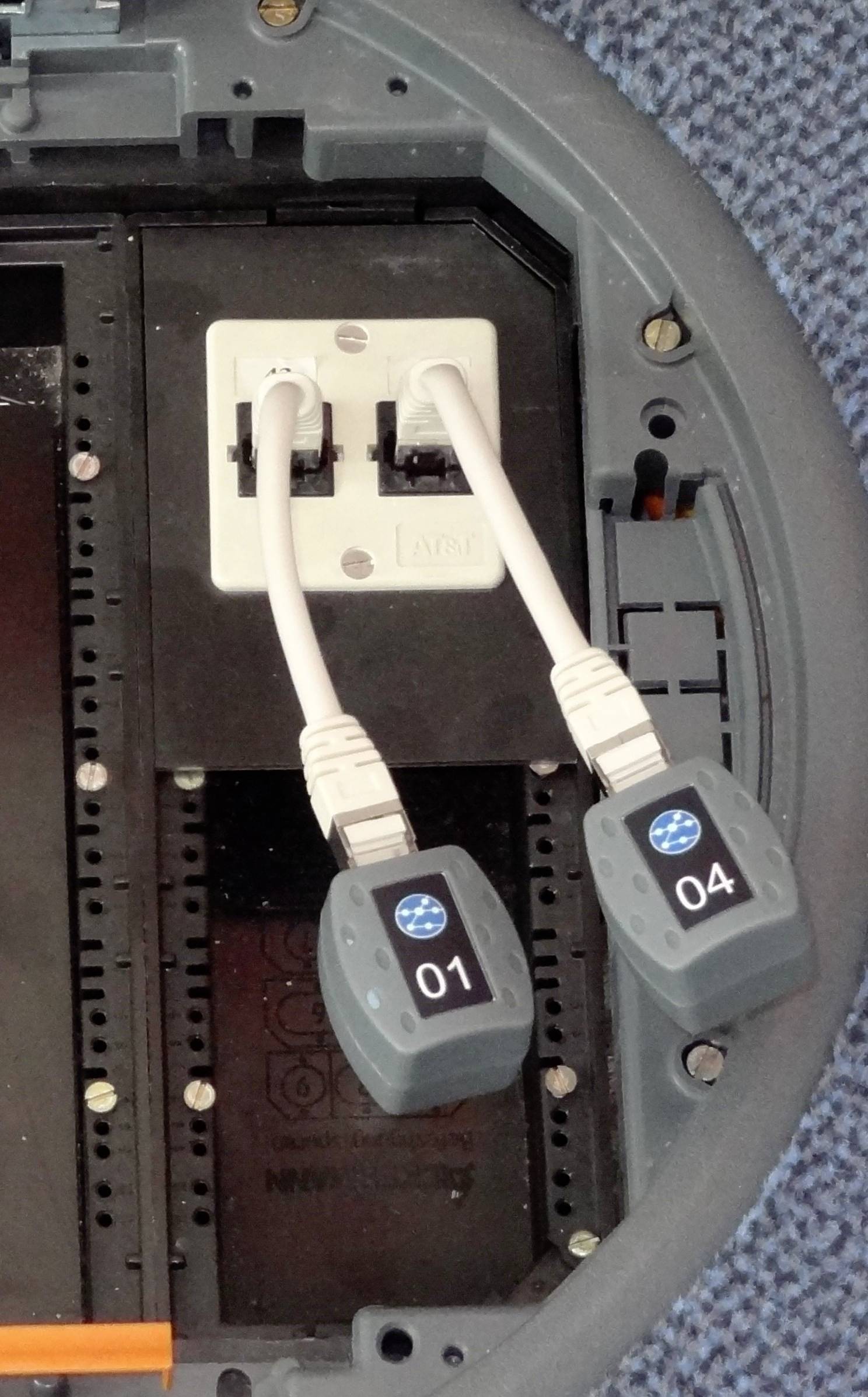 Zwei Netzwerkkabel sind an eine Wandbuchse angeschlossen, gekennzeichnet mit '01' und '04'. Sie verbinden Geräte mit einem Netzwerk.