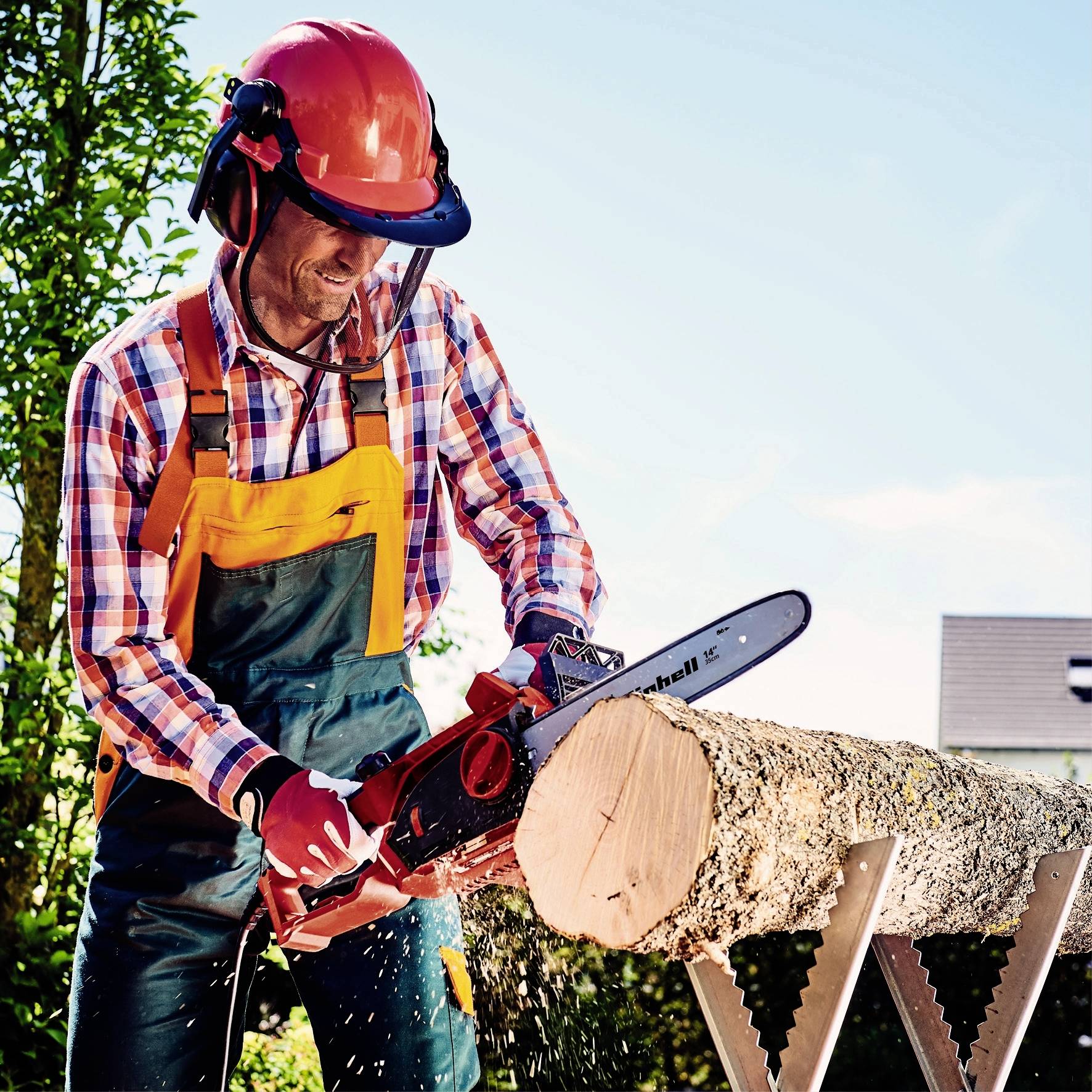 Eine Person mit Schutzkleidung und Helm schneidet einen Baumstamm mit einer Kettensäge auf einem Sägebock im Freien.
