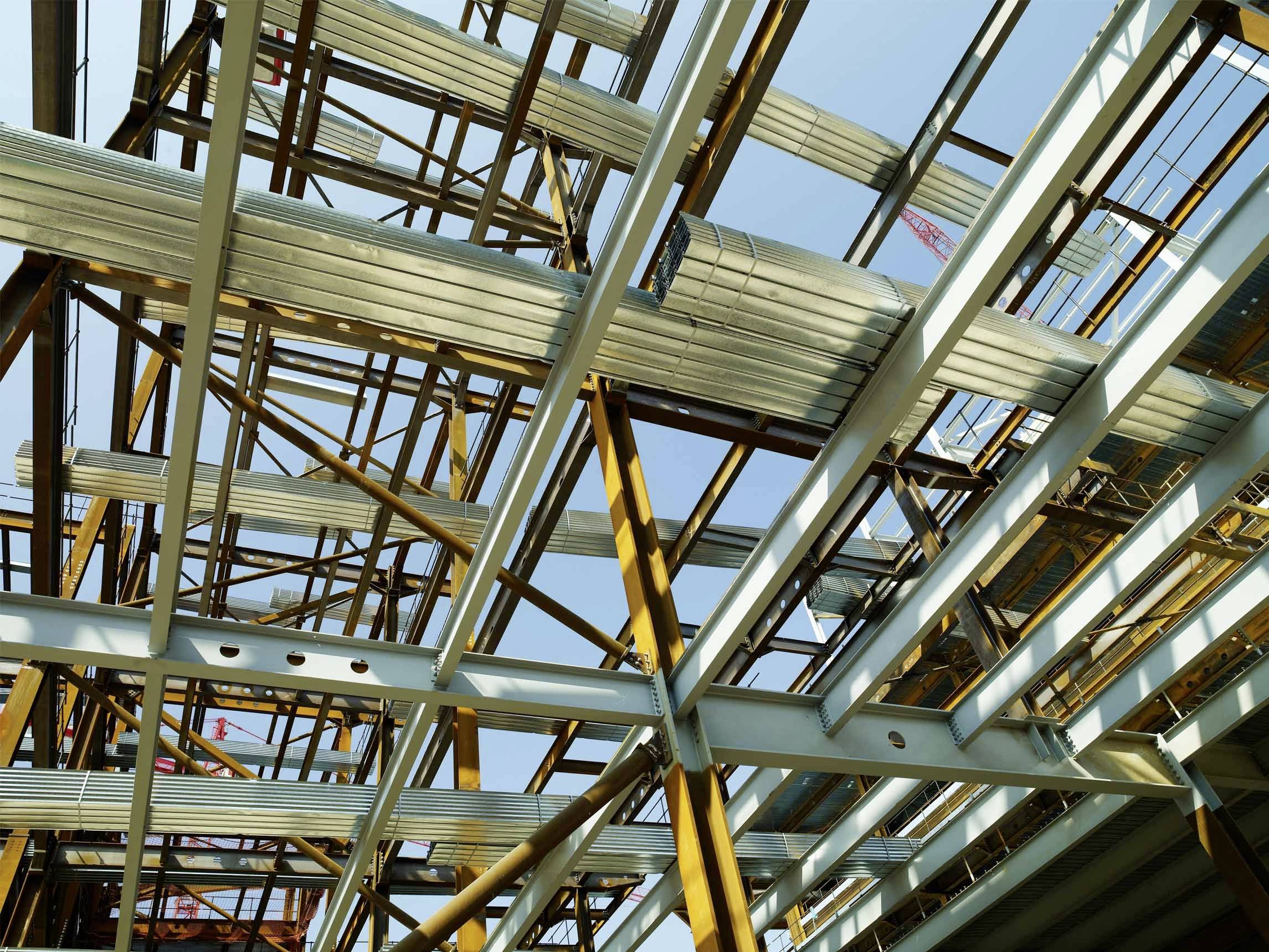 Metallgerüst einer Baustelle gegen blauen Himmel. Die Struktur zeigt komplexe Querstreben und vertikale Balken aus Stahl.