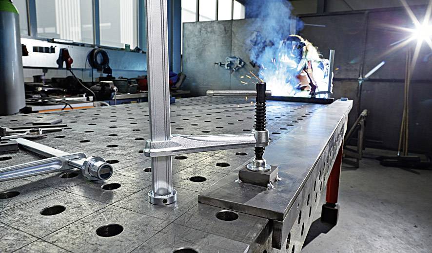 Person beim Schweißen in einer Werkstatt, Funken fliegen, Werkzeuge auf einem Metalltisch.