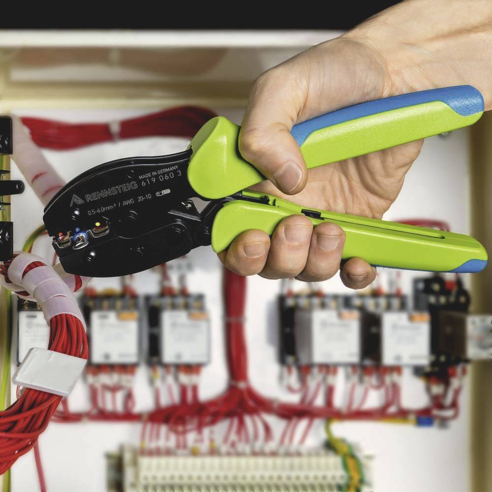 Eine Hand benutzt eine grüne Kabelschneidzange, um Drähte in einem Schaltschrank zu crimpen, umgeben von roten Kabeln und elektrischen Bauteilen.