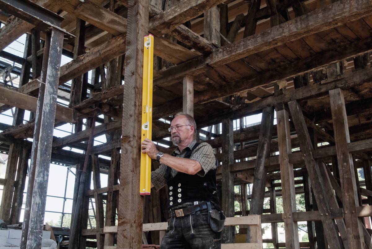 Ein Zimmermann arbeitet mit einer Wasserwaage an einem Holzbalken in einem halbfertigen Gebäude, um die Struktur ordentlich auszurichten.