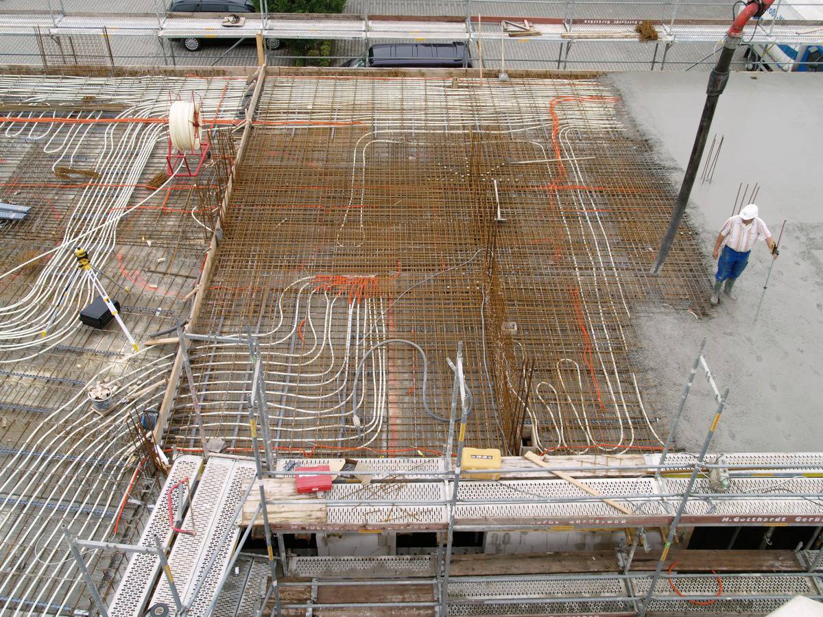 Bauarbeiter auf einer Baustelle, wo der Boden mit Stahlgitter und Heizungsschlangen vorbereitet wird. Beton wird gegossen.