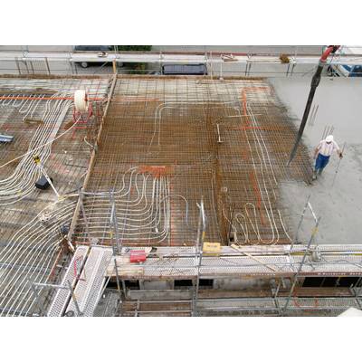 Bauarbeiter auf einer Baustelle, wo der Boden mit Stahlgitter und Heizungsschlangen vorbereitet wird. Beton wird gegossen.