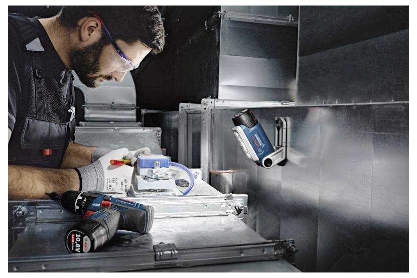 Techniker mit Sicherheitsbrille und Handschuhen, der eine kompakte Inspektionskamera an einem metallischen Lüftungskanal bedient und sich auf die Steuerung konzentriert.