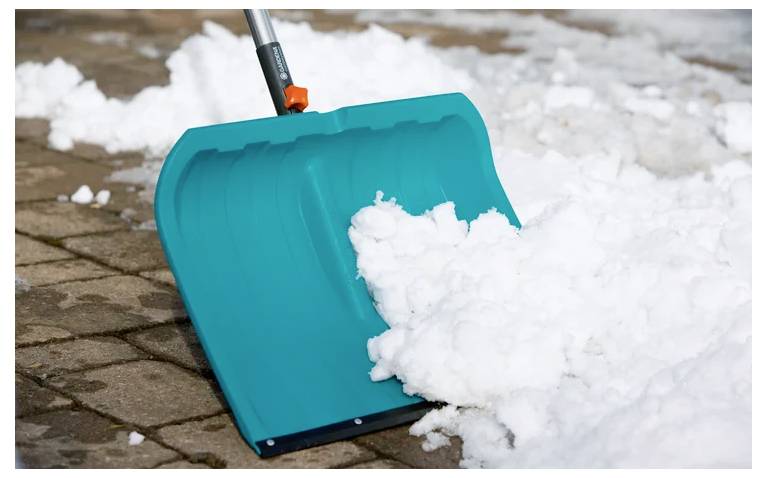 Eine blaue Schneeschaufel räumt Schnee von einem Backsteeinpfad.