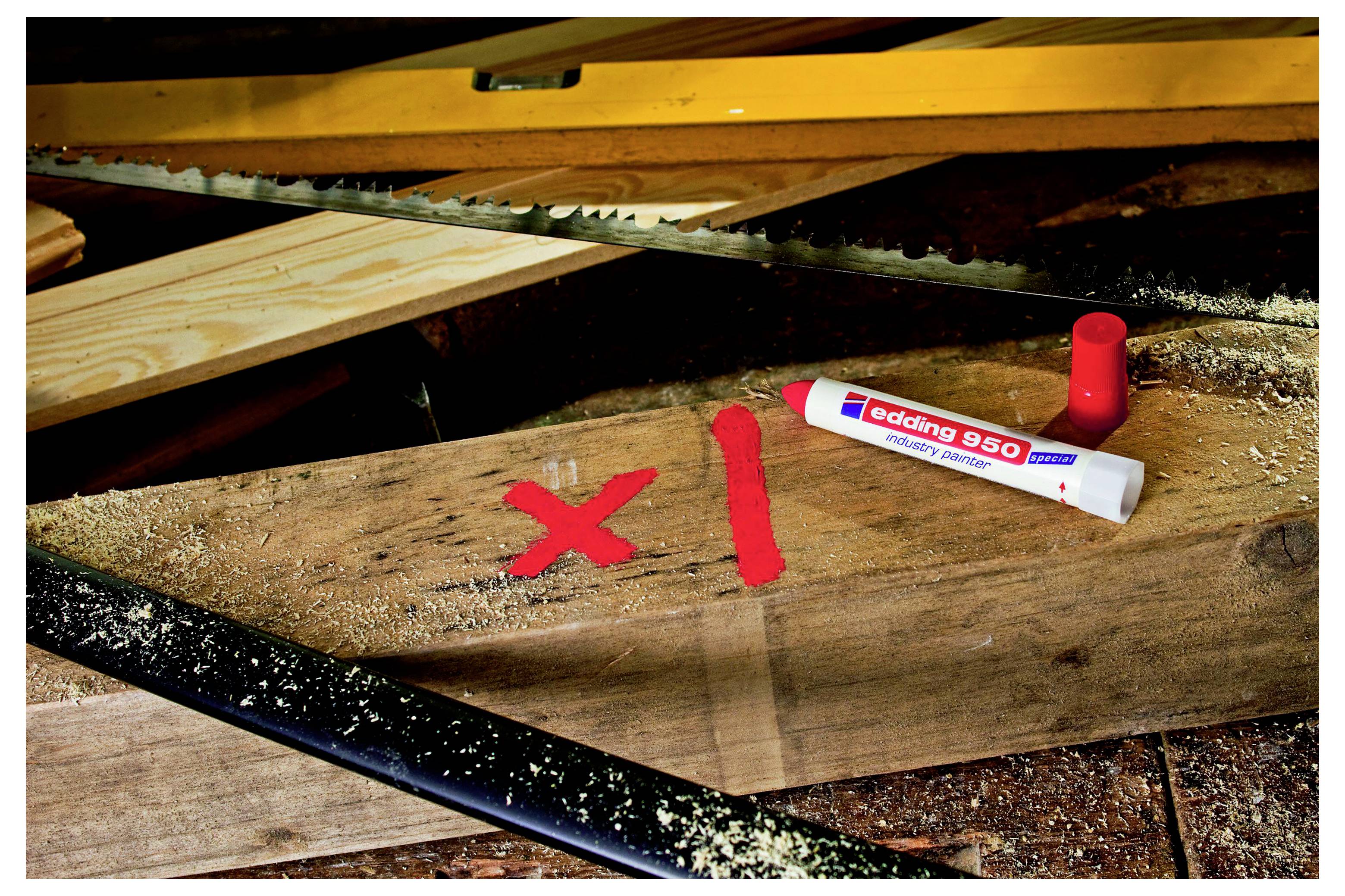 Holzbrett auf einem Sägetisch mit roter Farbe markiert, mit einem Edding 850 Lackmarker und Kappe in der Nähe in einer Werkstattumgebung.