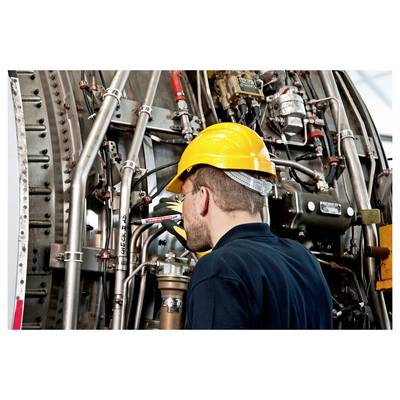 Arbeiter in gelbem Schutzhelm inspiziert eine dichte Industriemaschine mit Rohren und Ventilen.