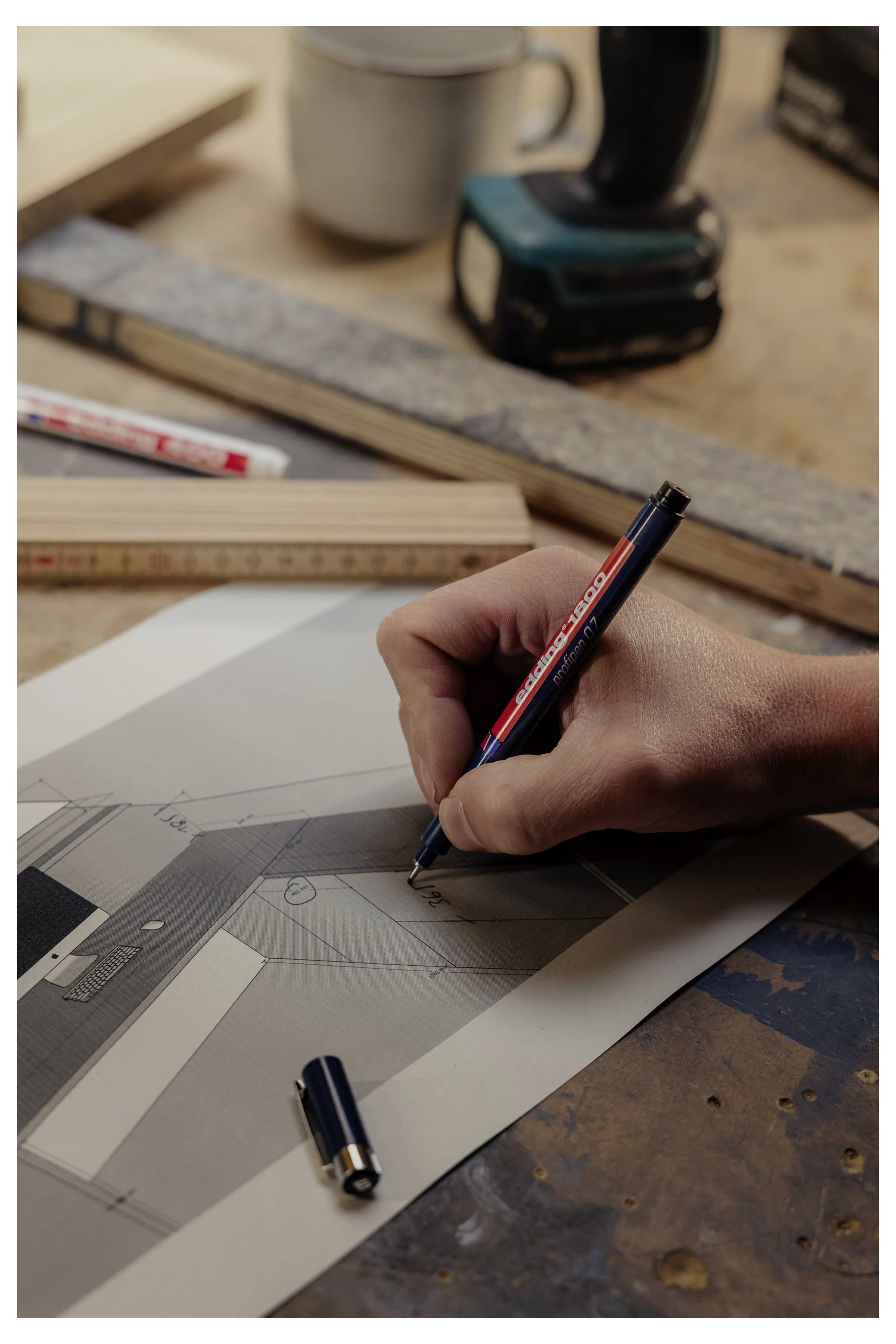 Handzeichnung eines Architekturplans auf Papier mit einem Bleistift, dargestellt auf einem Arbeitstisch mit Lineal und Zeichnungswerkzeugen.