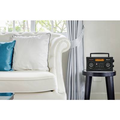 Ein elegantes Wohnzimmer mit weißem Sofa und blauem Kissen. Rechts steht auf einem kleinen Tisch ein schwarzes Radio mit Display.