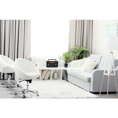 Helles Wohnzimmer mit grauem Sofa, zwei weißen Stühlen, einem Couchtisch mit Radio und Pflanzen vor einem großen Fenster mit Vorhängen.