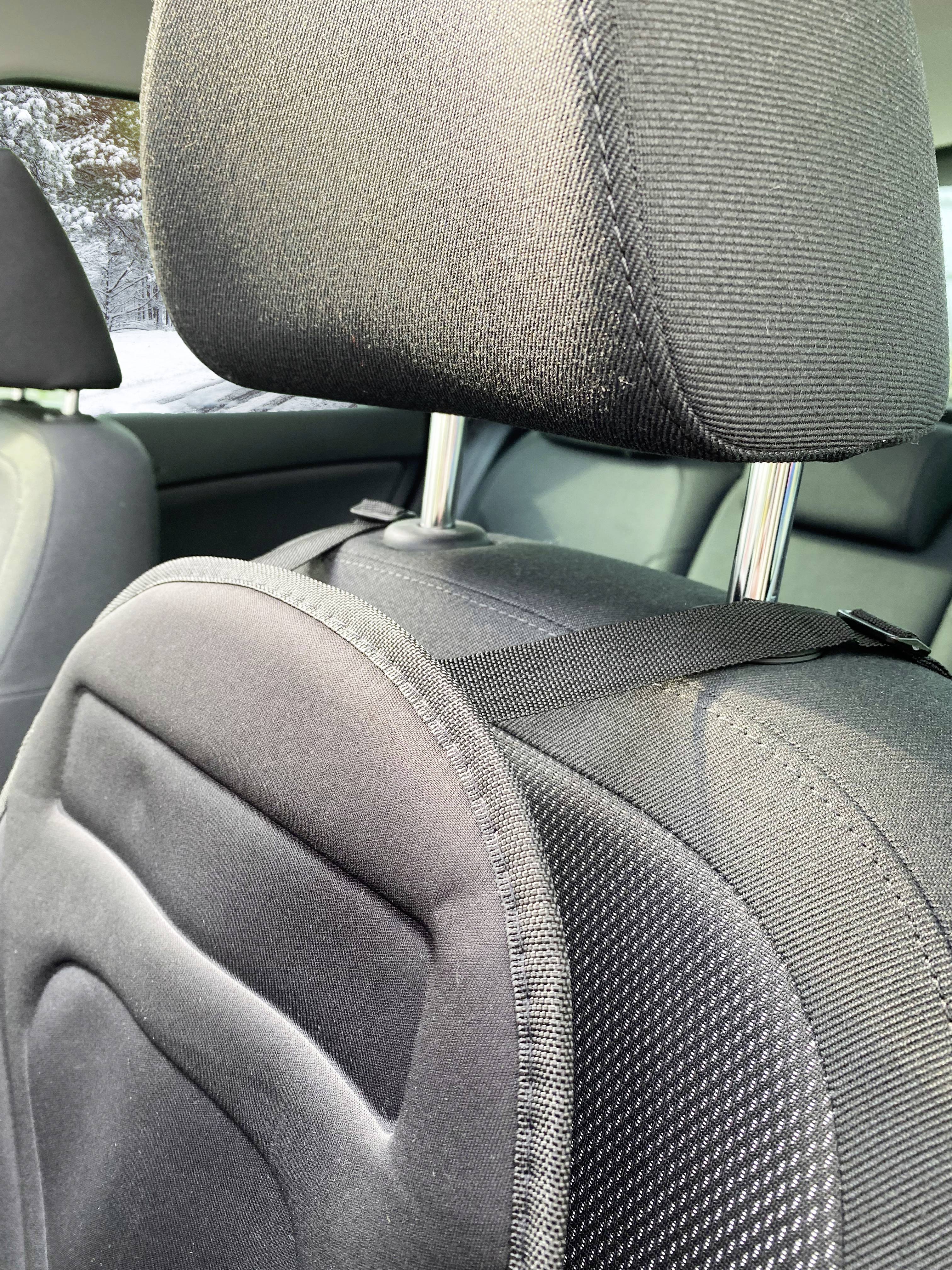 Rückansicht eines Autositzes mit hochgeklapptem schwarzen Kopfstützenpolster, gesehen bei Tageslicht.