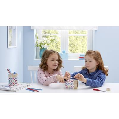 Zwei Kinder sitzen an einem Tisch in einem hellen Raum und basteln gemeinsam. Auf dem Tisch liegen Buntstifte und Bastelmaterial.