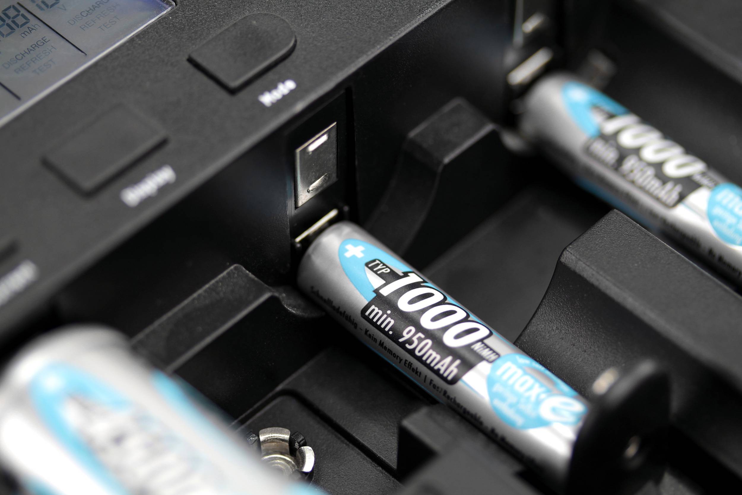 Nahaufnahme eines Batterieladegeräts mit eingelegten AA-Akkus, die aufgeladen werden. Der Ladezustand wird über ein Display angezeigt.