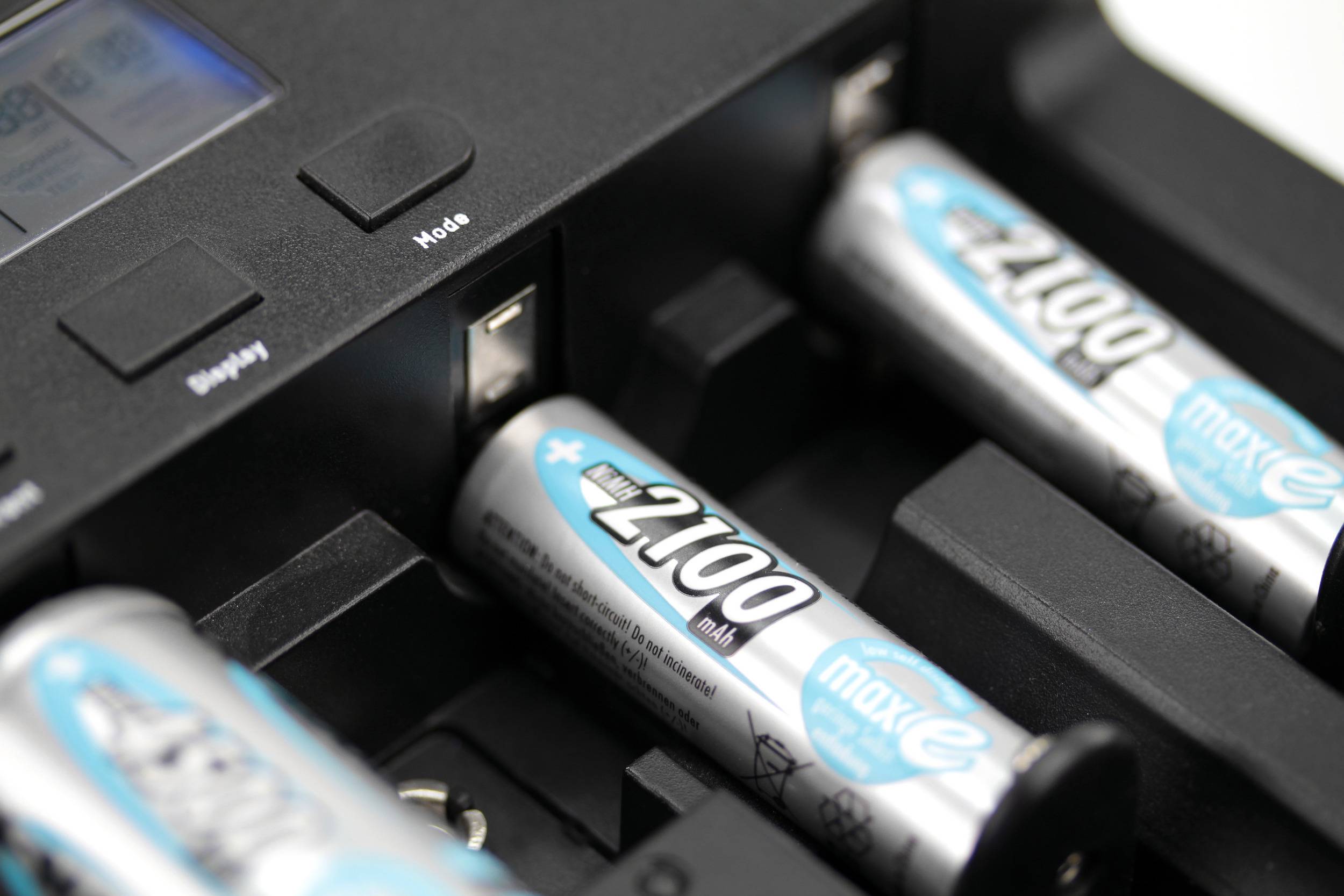 Vier AA-Batterien werden in einem Ladegerät geladen. Zwei Batterien im Vordergrund, eine und ein Steuerdisplay unscharf im Hintergrund.