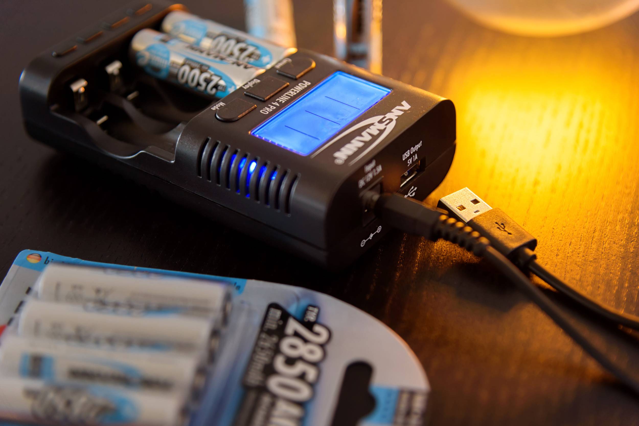 Ein Ladegerät lädt vier AA-Batterien auf, angezeigt durch einen leuchtenden digitalen Bildschirm. USB-Kabel angeschlossen.