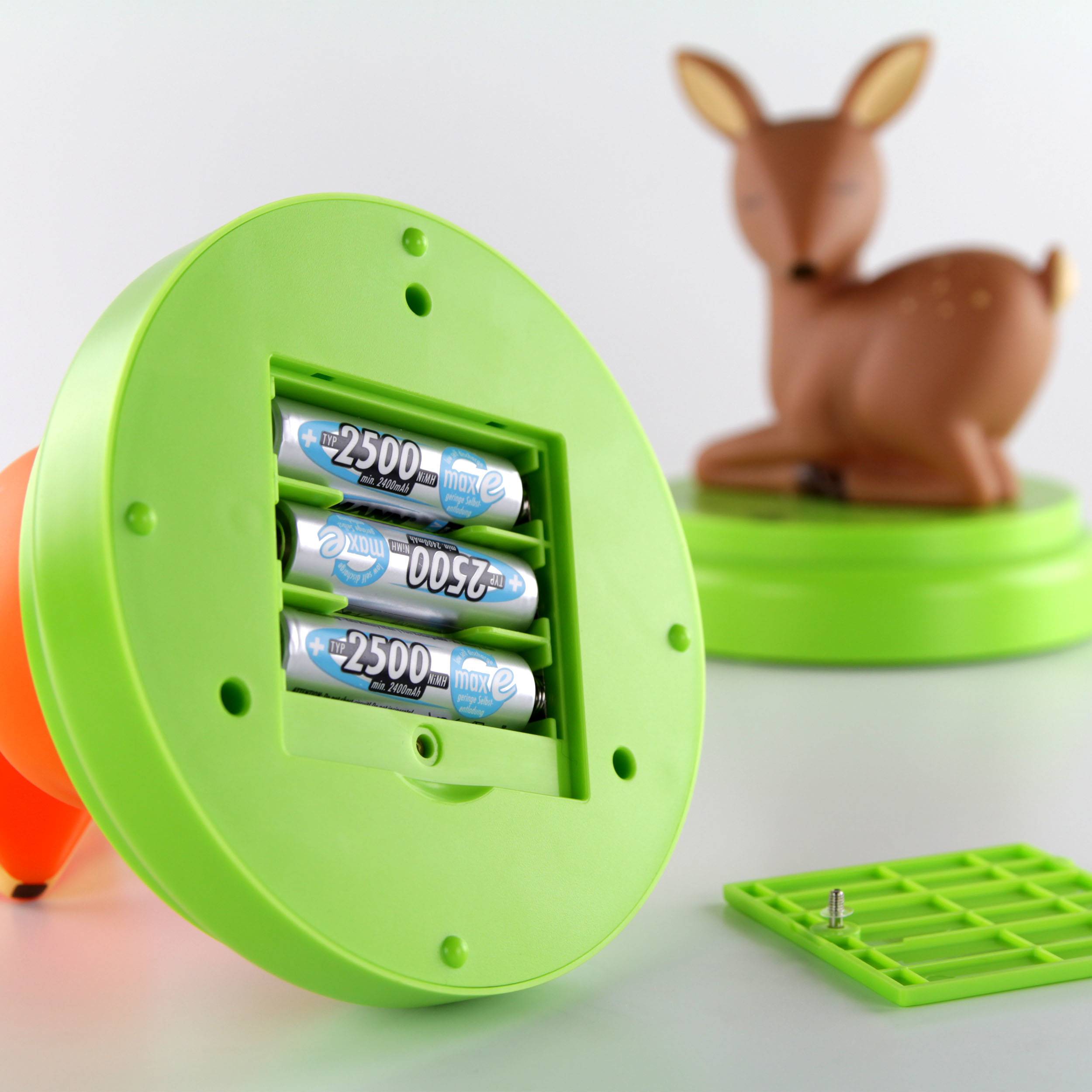 Batteriefach eines grünen Kunststoffgeräts, geöffnet. Dahinter unscharfe Kunststofffigur eines Rehs.