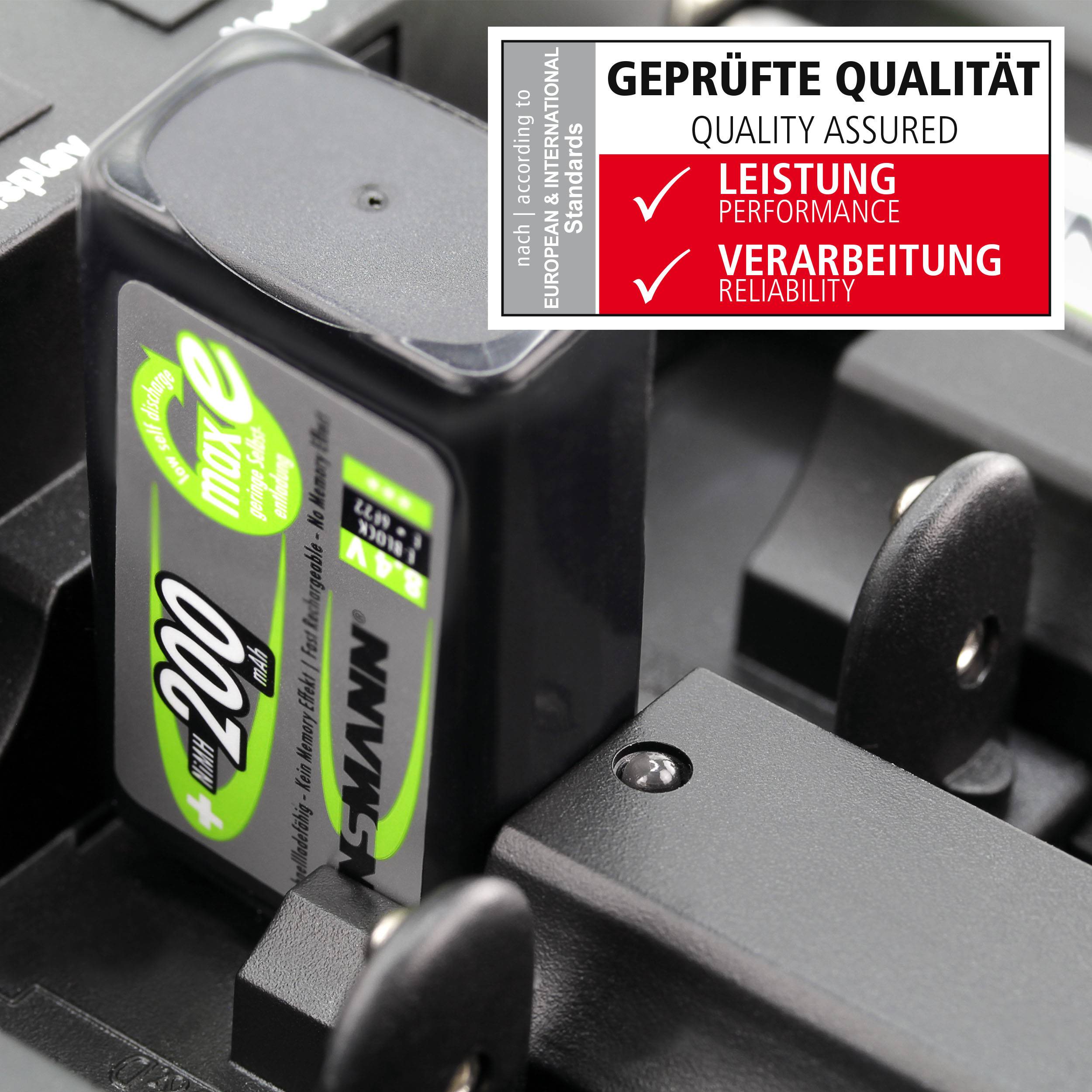 Ein schwarzes Batterieladegerät lädt zwei grüne Akkus der Marke ANSMANN. Oben rechts ein Qualitätssiegel mit Aufschrift 'Geprüfte Qualität, Leistung, Verarbeitung'.