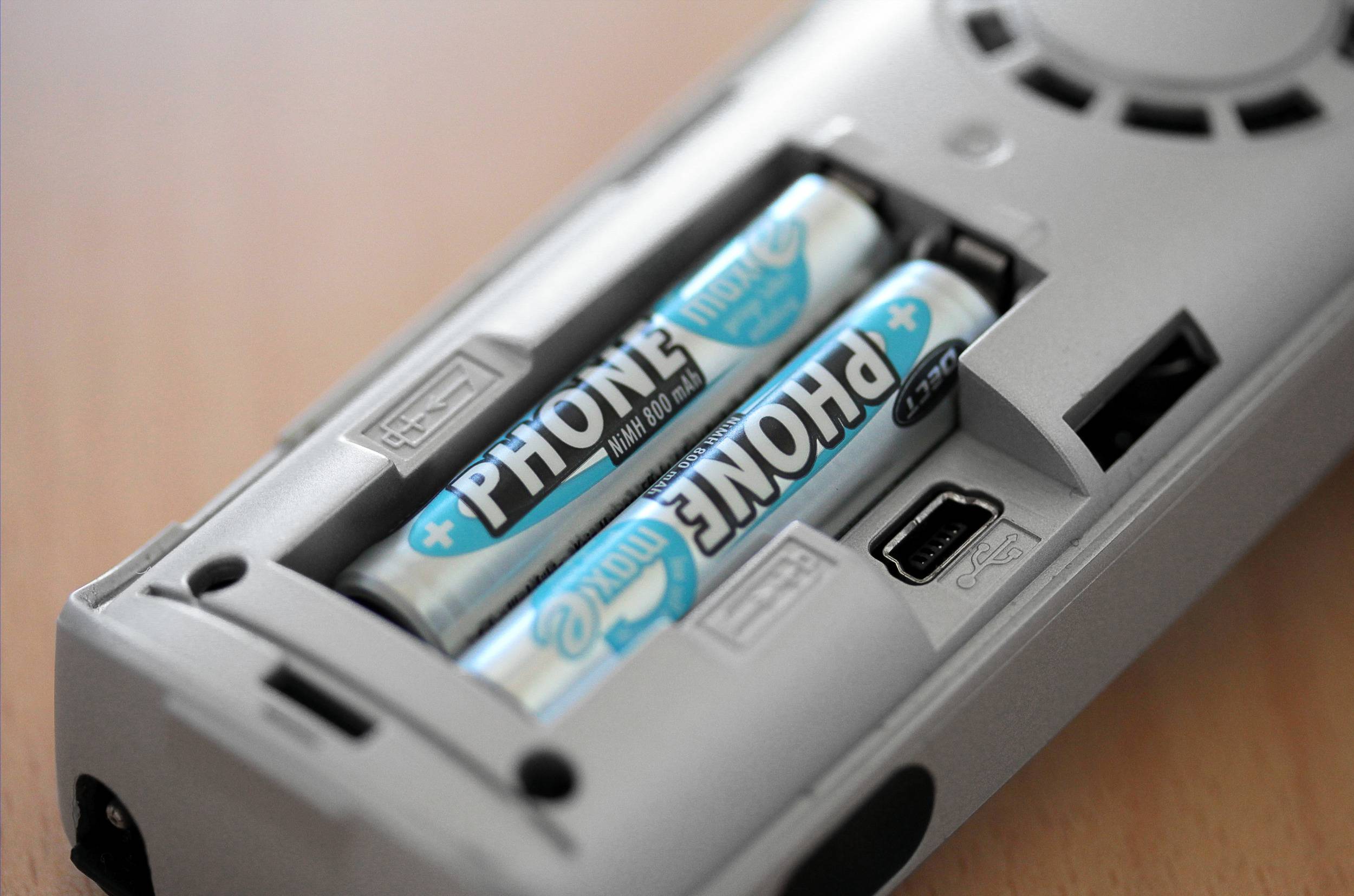 'Nahaufnahme von zwei AA-Batterien in einem Batteriefach. Die Batterien sind blau und mit der Aufschrift "PHONE" bedruckt.'