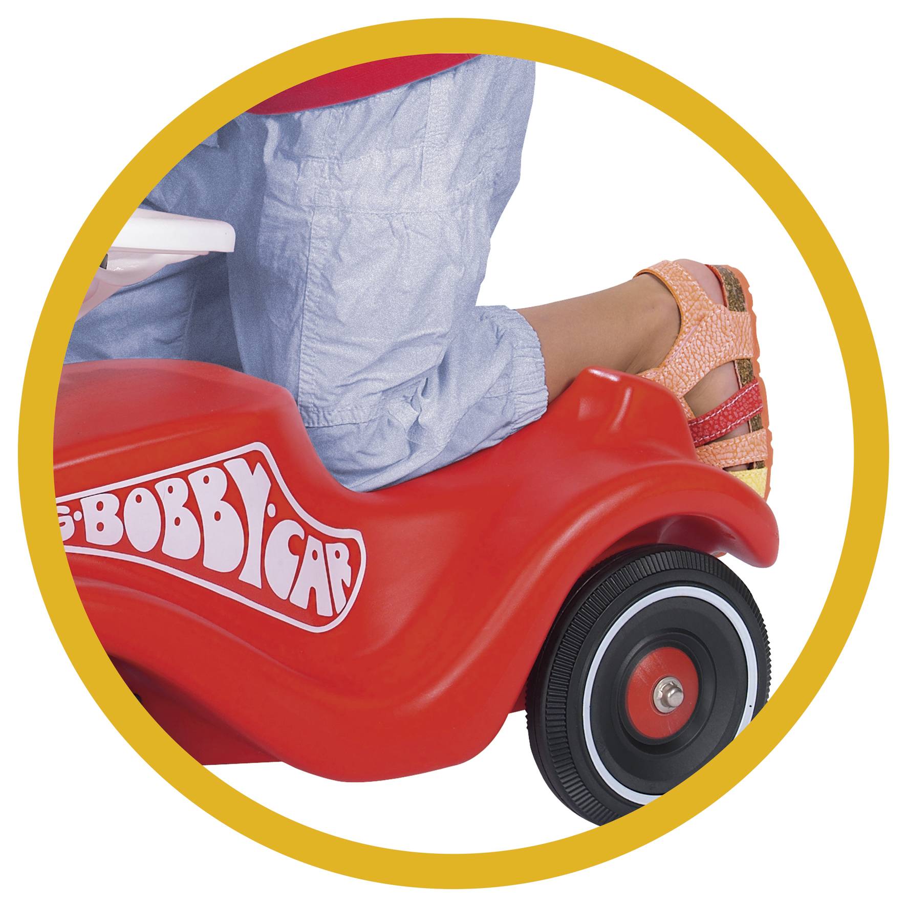 Ein Kind trägt korallenfarbene Sandalen und fährt auf einem roten Spielzeugauto mit der Aufschrift 'Bobby-Car'.