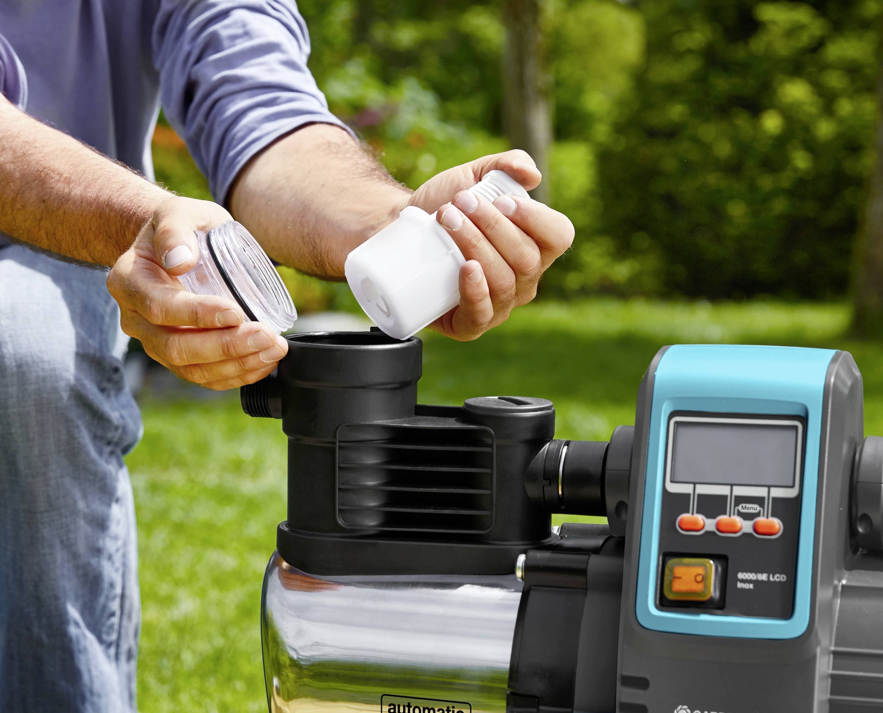 Person installiert oder wartet eine Gartenpumpe im Freien. Nahaufnahme von Händen beim Befüllen oder Prüfen eines Behälters der Pumpe.