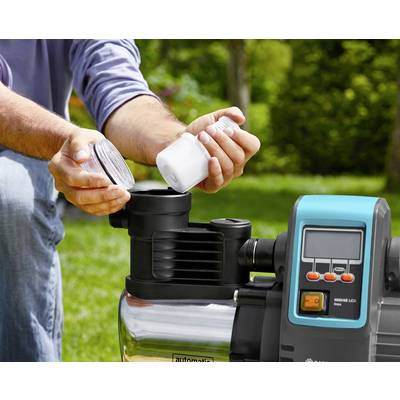 Person installiert oder wartet eine Gartenpumpe im Freien. Nahaufnahme von Händen beim Befüllen oder Prüfen eines Behälters der Pumpe.