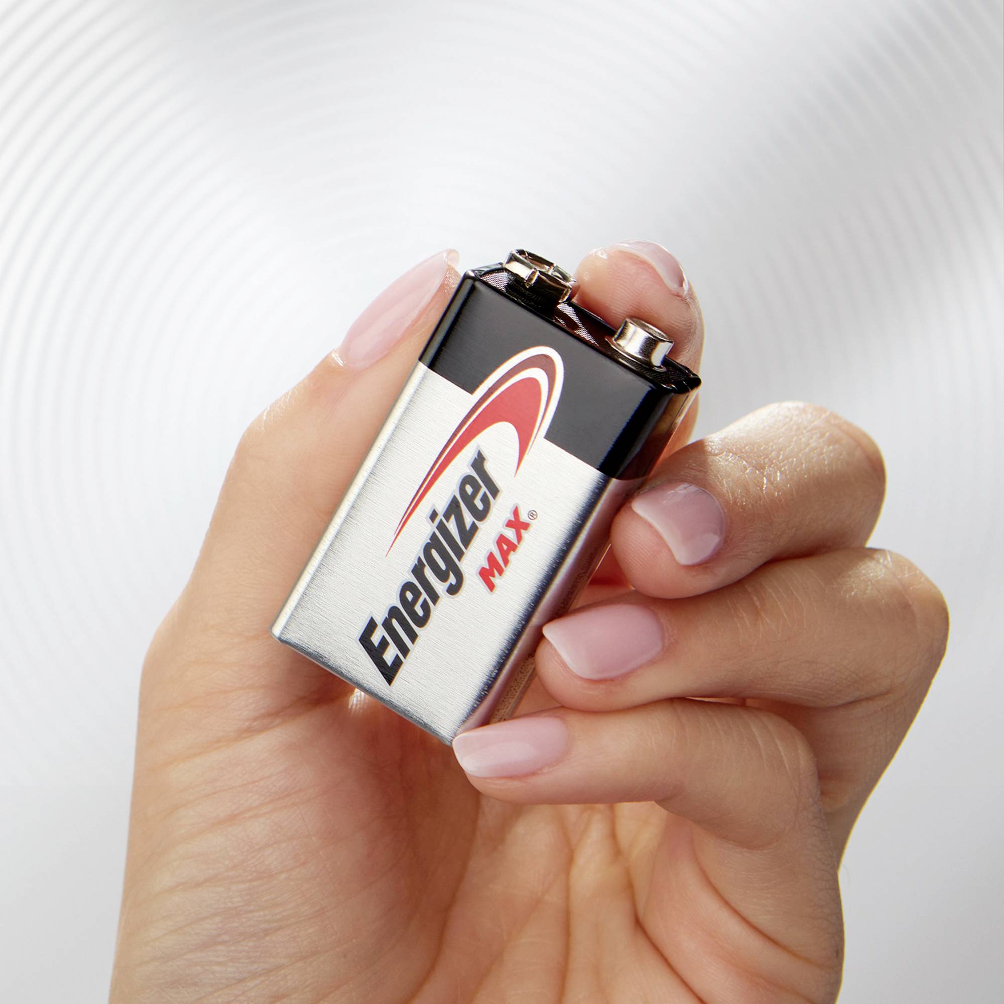 Eine Hand hält eine 9-Volt 'Energizer Max'-Batterie. Die Batterieverpackung ist silbern mit rotem Logo.