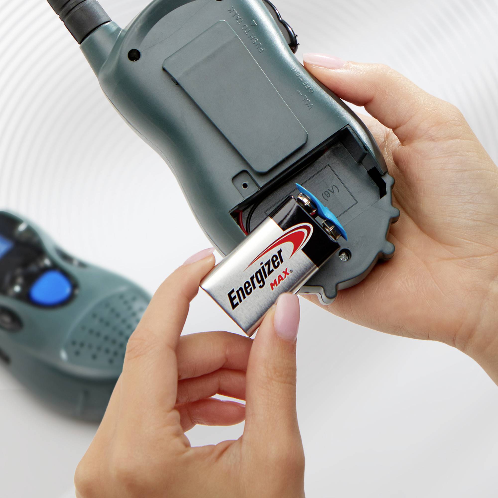 Eine Person hält eine große Batterie, um sie in ein Walkie-Talkie einzusetzen, das eine offene Batteriefachabdeckung zeigt.