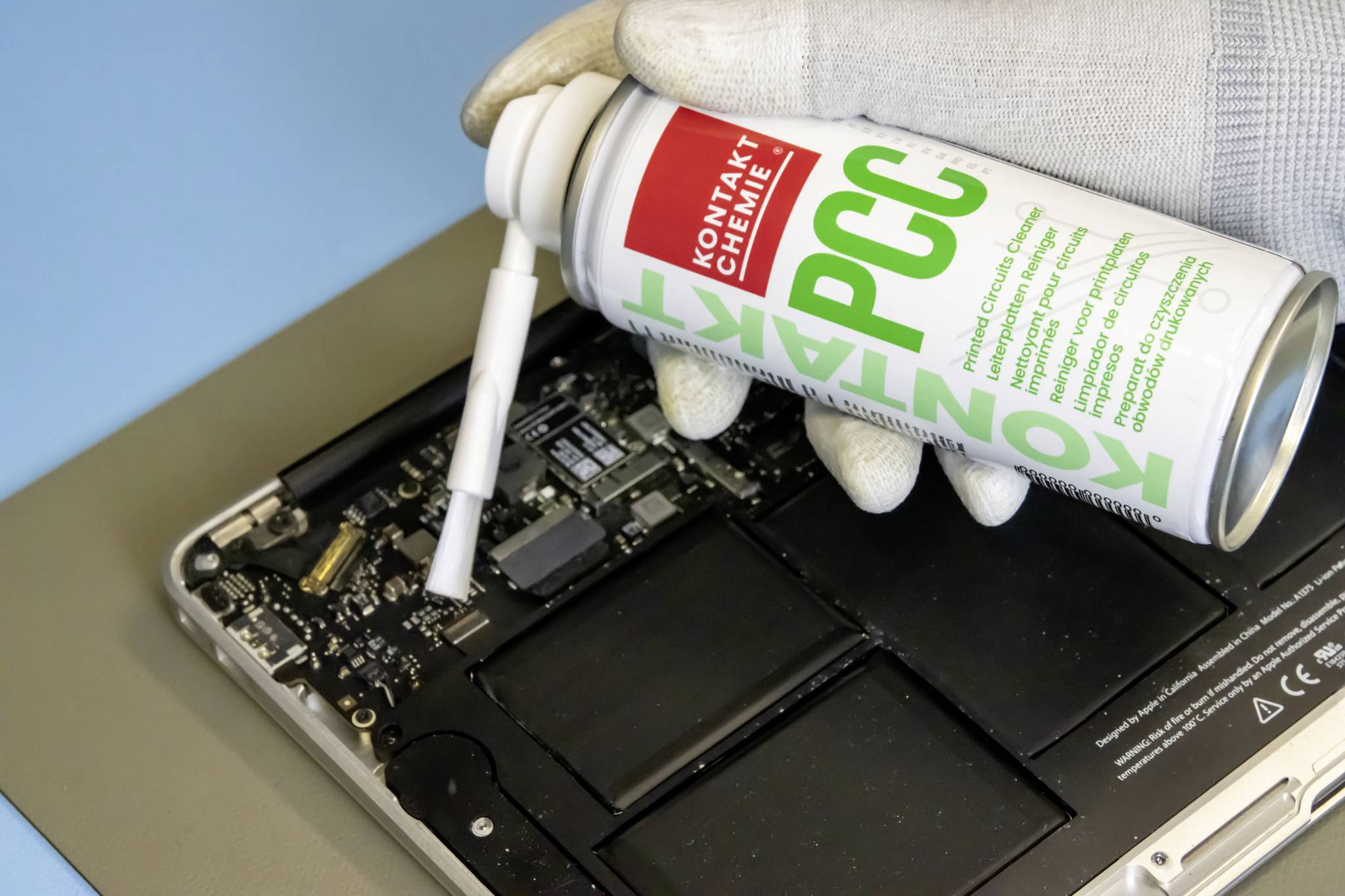 Ein Computertechniker reinigt eine geöffnete Laptop-Hardware mit Druckluft, trägt Handschuhe. Reinigung und Wartung der Technik.