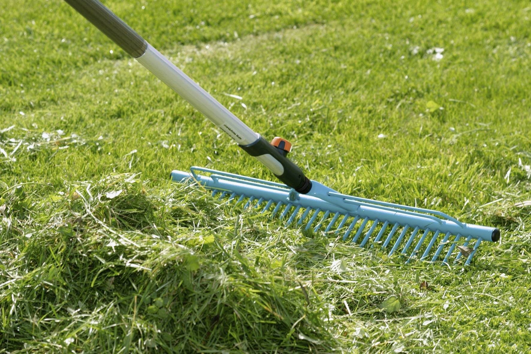 Eine blaue Harke bewegt frisch geschnittenes Gras auf einer grünen Rasenfläche.