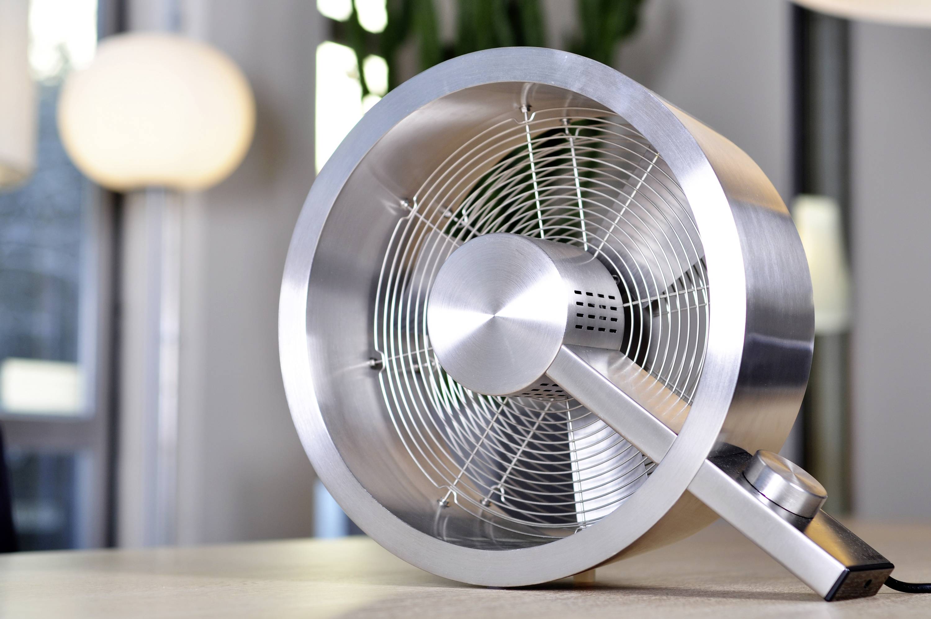 Ein moderner Tischventilator aus Metall steht auf einem Tisch in einem hellen Raum.