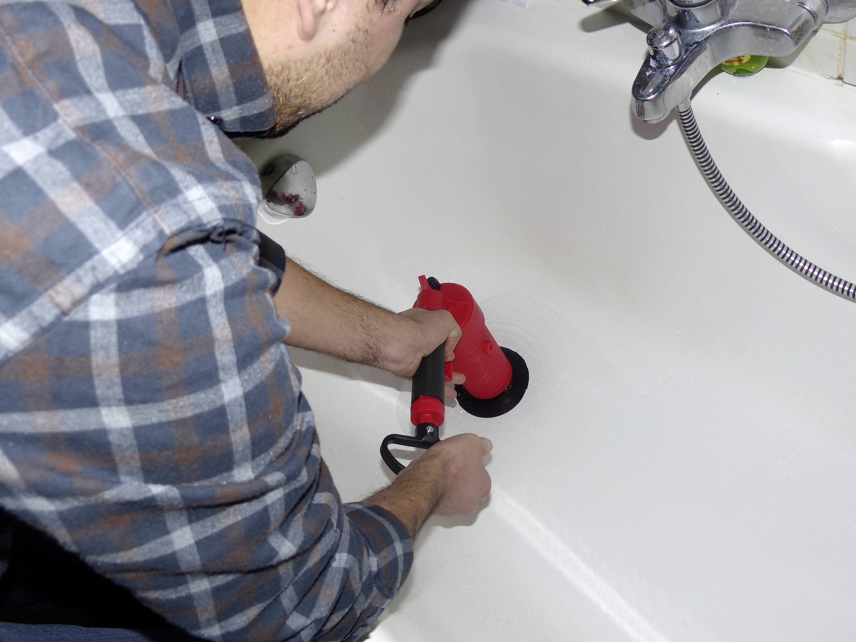 Eine Person reinigt eine Badewanne mit einem roten, handbetriebenen Reinigungswerkzeug.