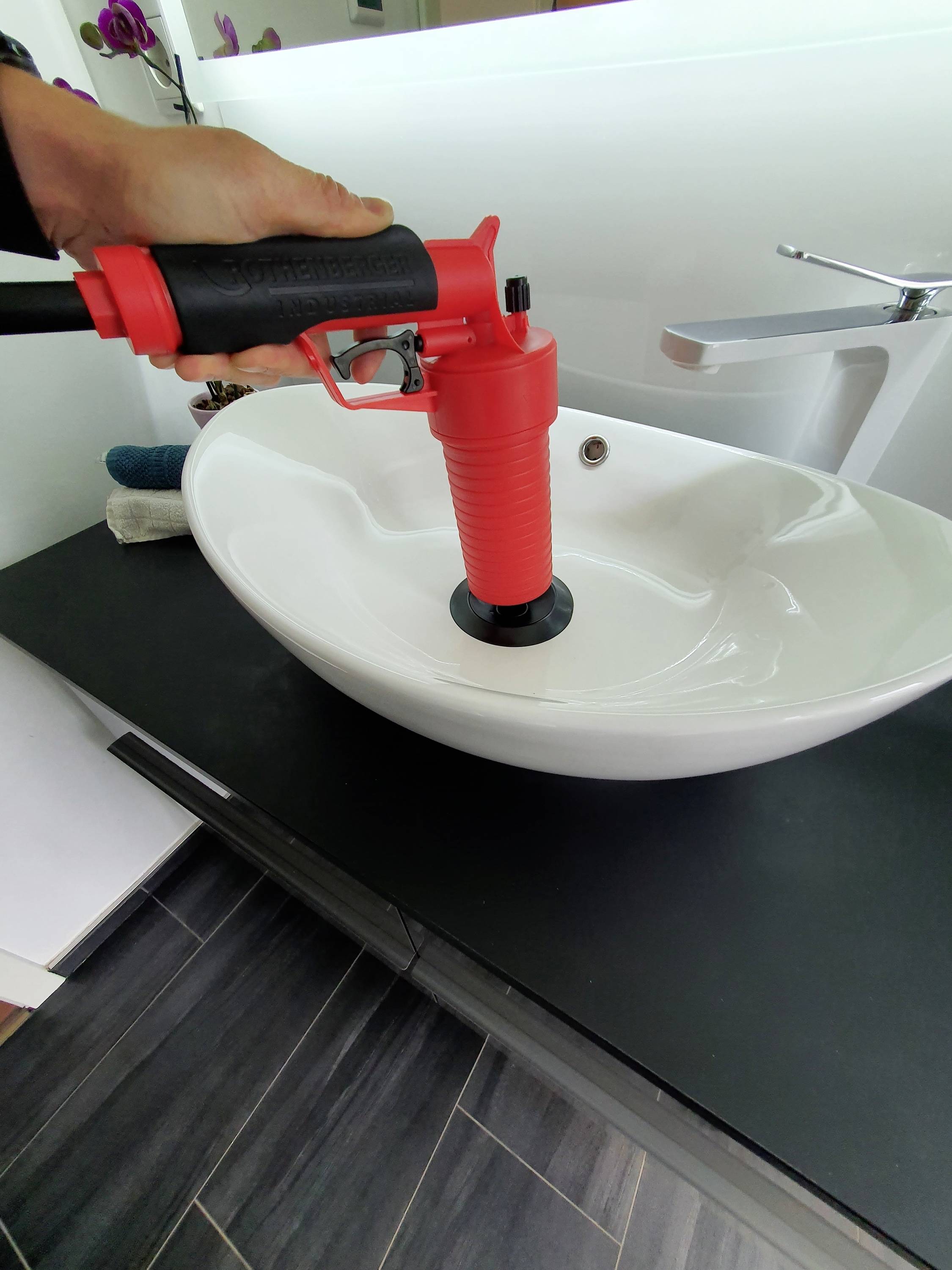 Eine Hand benutzt eine rote Saugglocke, um ein ovales Waschbecken in einem modernen Badezimmer zu entstopfen.