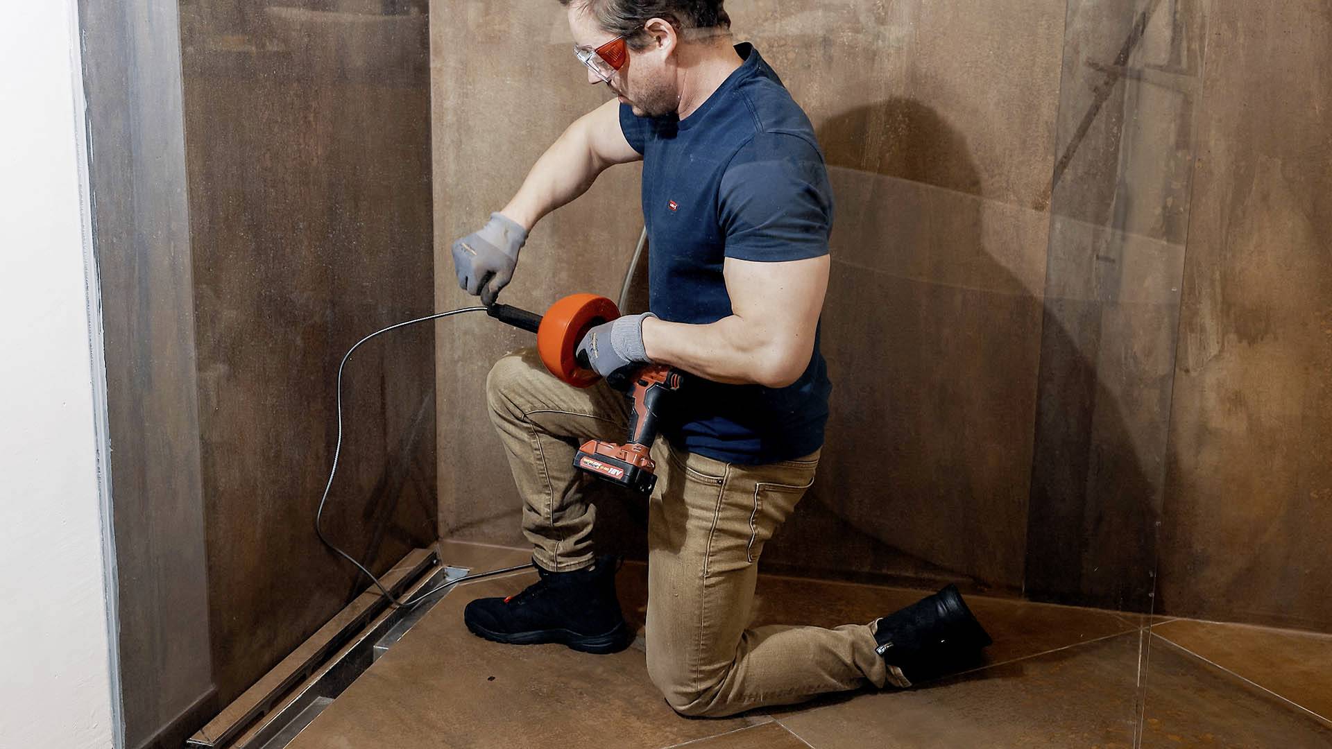 Ein Mann arbeitet in einem Raum und verwendet ein Werkzeug zum Bearbeiten eines Bodens. Er trägt Schutzbrille und Handschuhe.