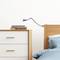 Ein schlicht eingerichtetes Schlafzimmer mit einem Holzbett, blauer Bettwäsche, einer weißen Kommode und einer Leseleuchte an der Wand.