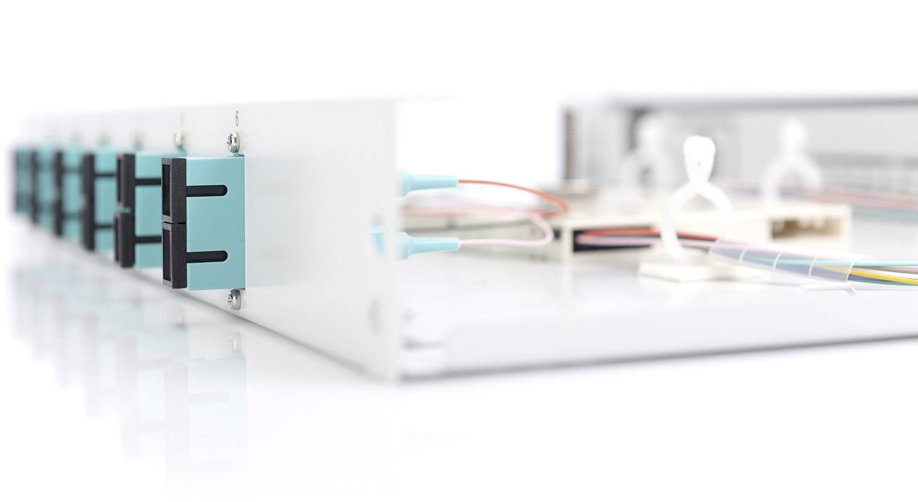 Faseroptik-Verkabelung in einem Netzwerkgerät, mit blau markierten Anschlüssen und farbigen Kabeln, die auf einer weißen Oberfläche liegen.