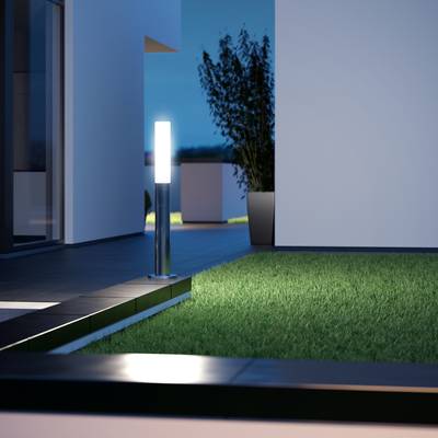 Eine beleuchtete moderne Terrasse mit Rasenfläche, bepflanztem Topf und minimalistischem Gebäude im Hintergrund bei Dämmerung.