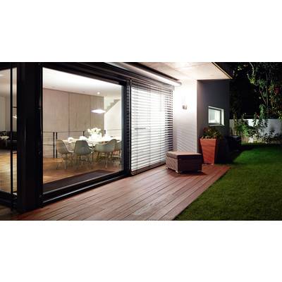 Ein modernes Wohnzimmer mit Glasfront, das in einen beleuchteten Garten mit Holzterrasse und Rasen übergeht.