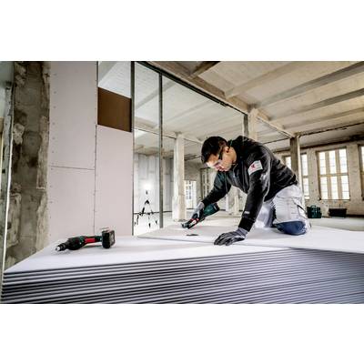 Ein Handwerker schneidet in einem Gebäudebauprojekt Trockenbauplatten. Er trägt Schutzbrille und arbeitet konzentriert mit einem Elektrowerkzeug.