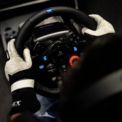 Eine Person mit Handschuhen hält ein Gaming-Lenkrad, das mit einem PlayStation-Logo versehen ist, bereit für eine Rennsimulation.