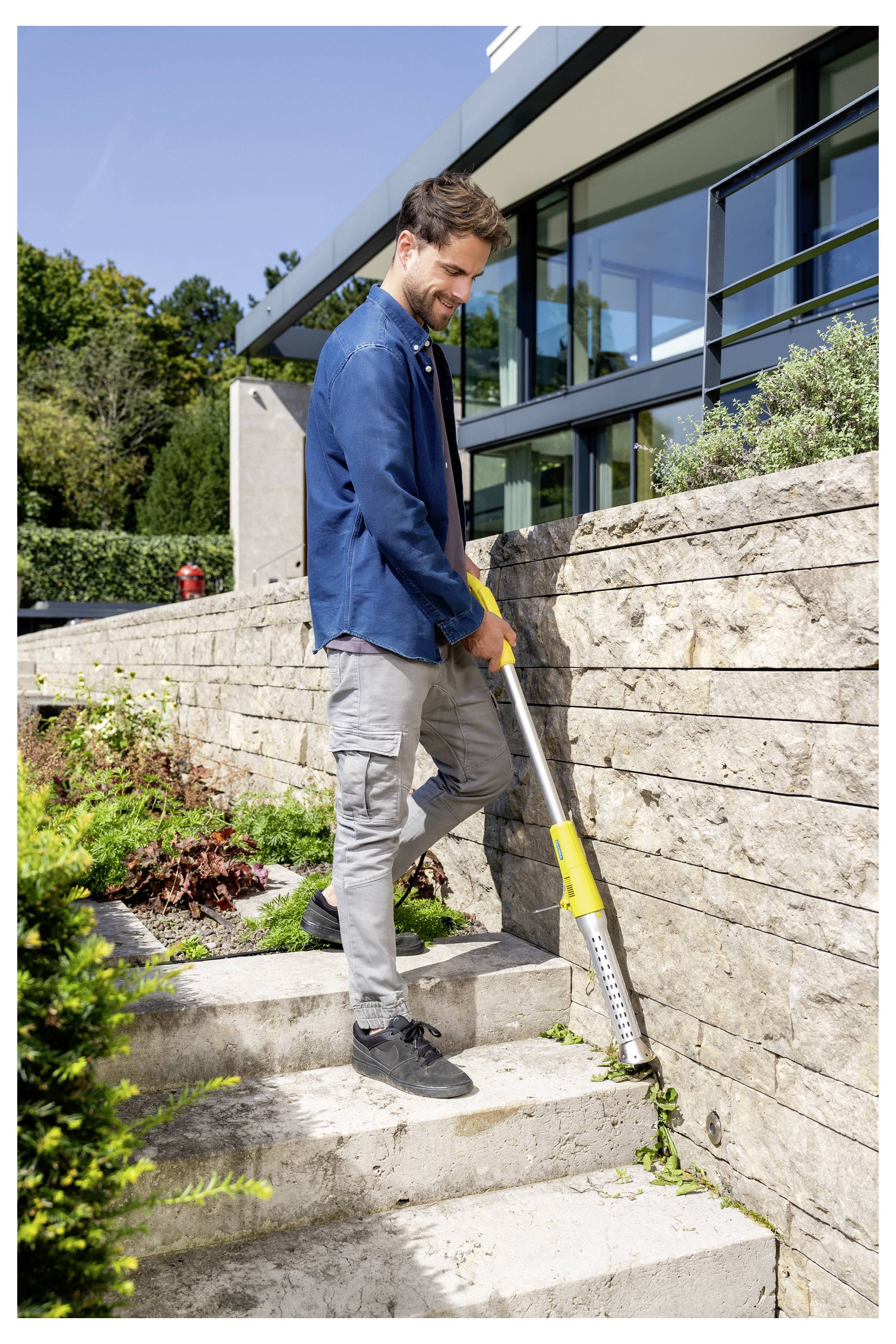 Mann, der einen Fadentrimmer auf Steinstufen neben einem modernen Haus und einer Gartenmauer benutzt.