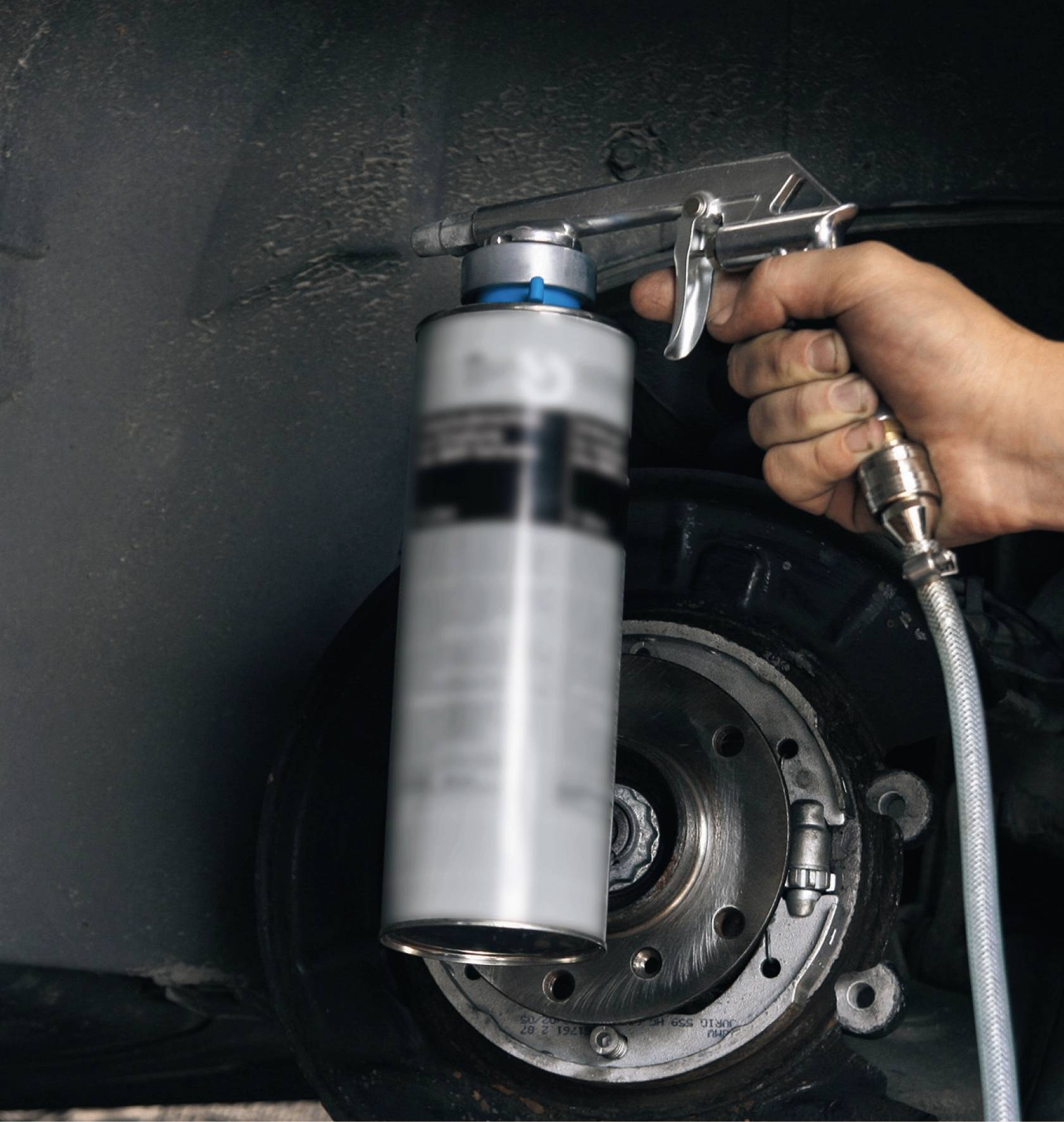 Eine Hand hält eine Sprühdose mit einer Pistolenhalterung in der Nähe eines Autoreifens, scheinbar zur Wartung oder Reinigung.