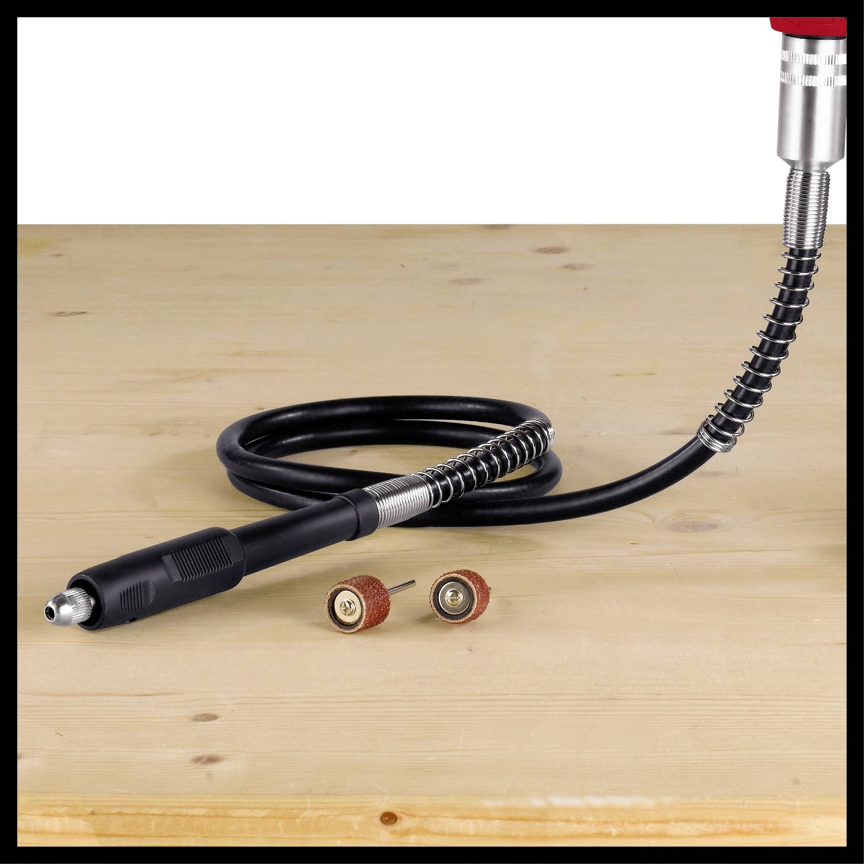 Ein Elektrowerkzeug auf einem Holztisch, umgeben von Düsenaufsätzen. Hauptteil zeigt ein spiralförmiges Kabel und austauschbare Köpfe.