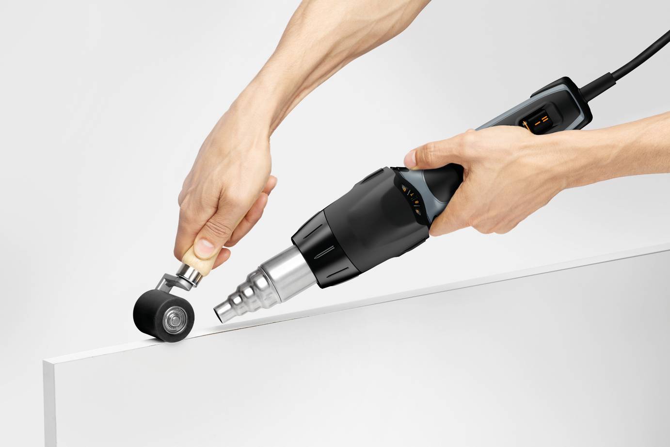 Eine Person bedient ein Heißluftgebläse, um eine Kunststoffplatte zu formen. Das Gebläse hat eine konische Düse, die auf den Plattenrand gerichtet ist.