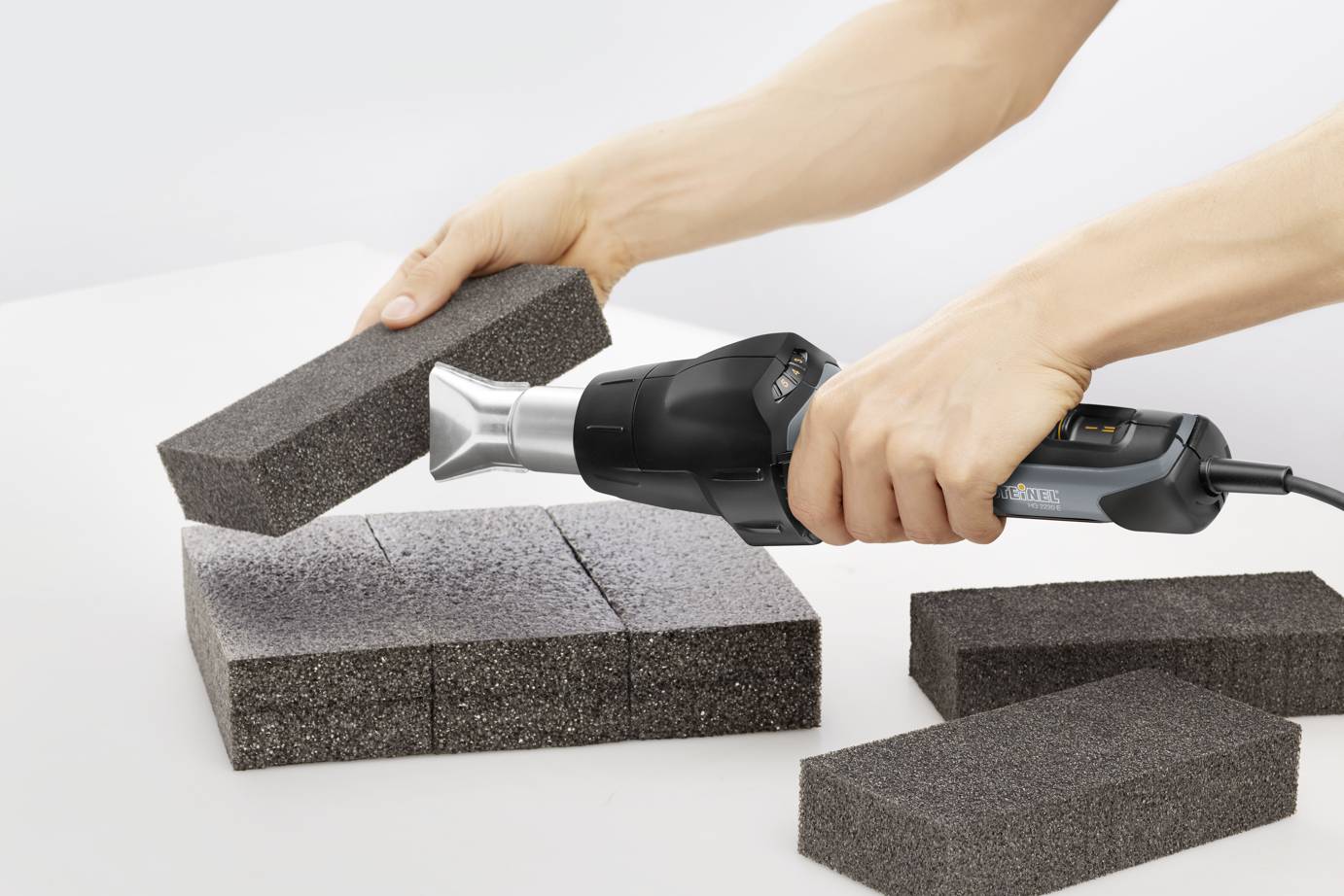 'Person hält Heißluftgebläse, das auf Schaumstoffziegel gerichtet ist, um sie zu formen oder zu bearbeiten.'