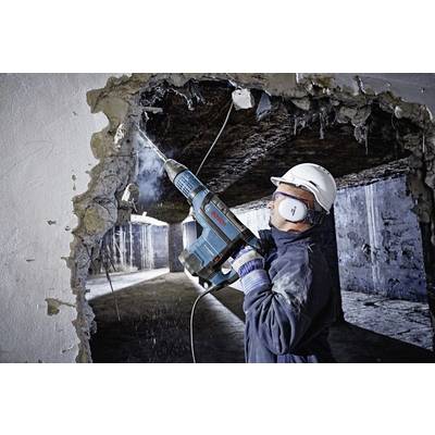Ein Bauarbeiter in Sicherheitsausrüstung verwendet ein Elektrowerkzeug, um eine Wand aus Beton zu durchbohren und eine Öffnung zwischen zwei Räumen zu schaffen.